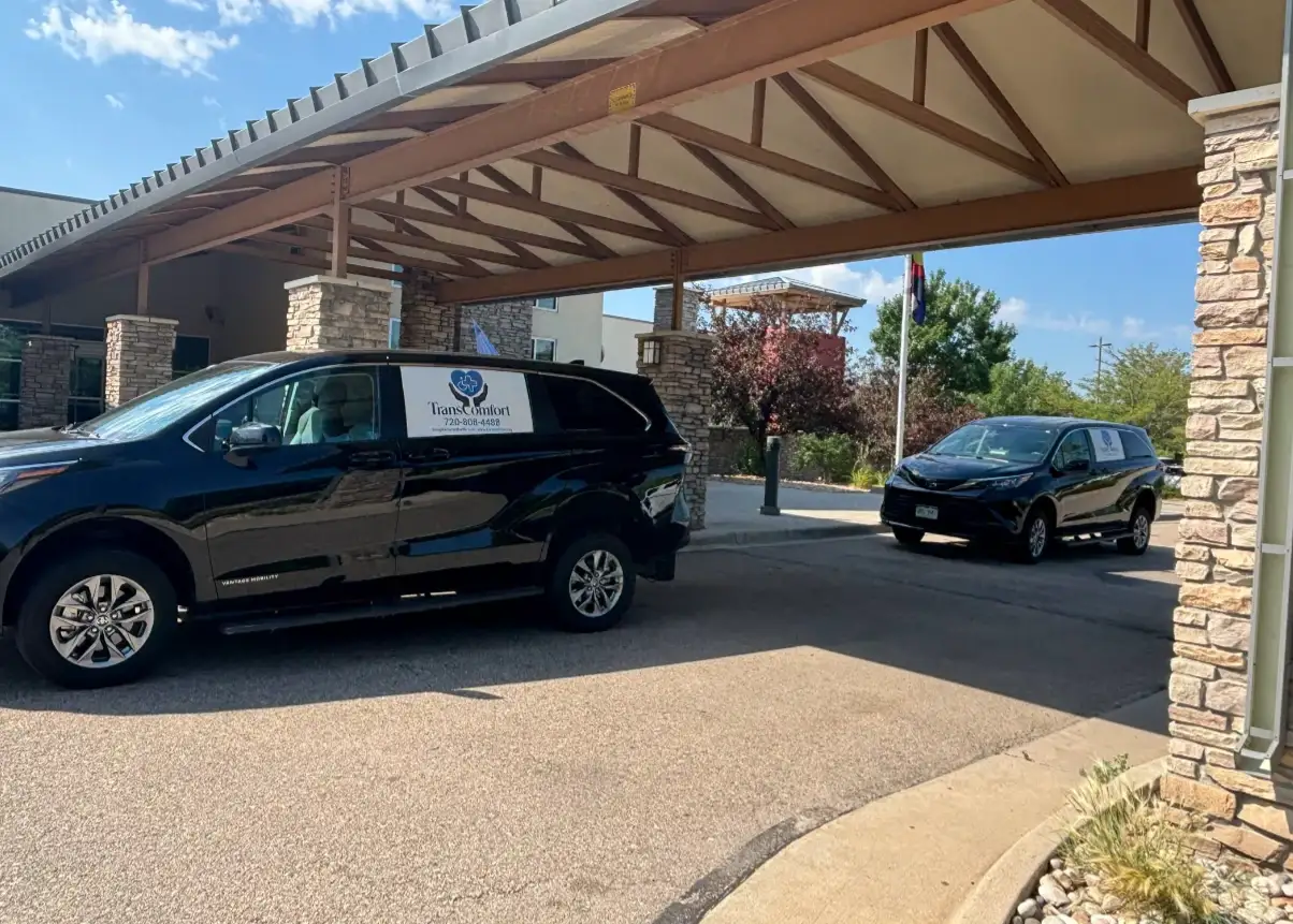 Two TransComfort accessible vans waiting under the covered entrance of a care facility.