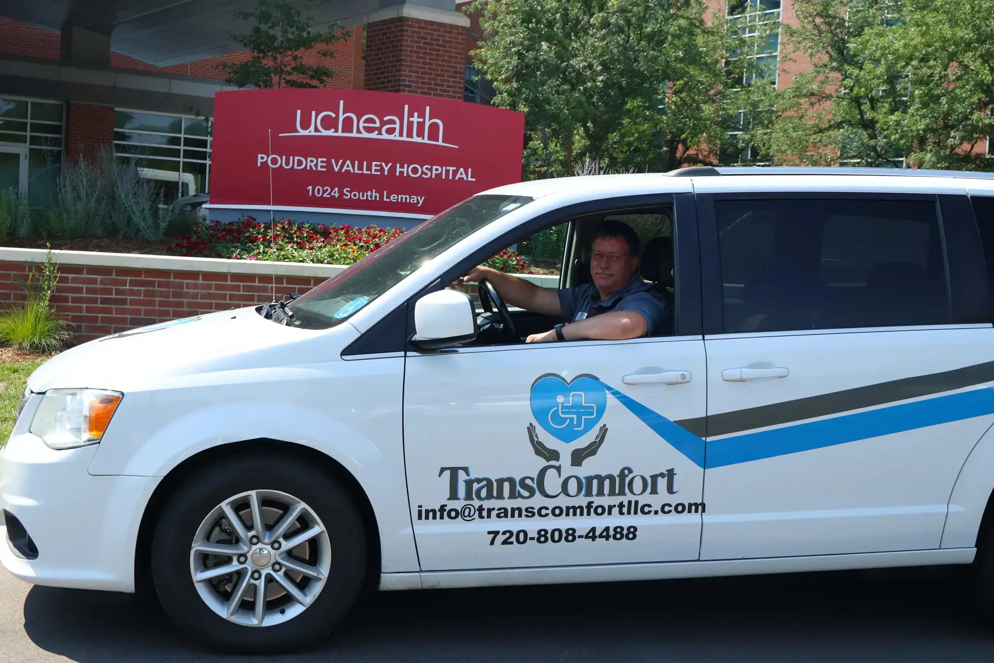 A TransComfort driver at the wheel of a white wheelchair-accessible van outside Poudre Valley Hospital.