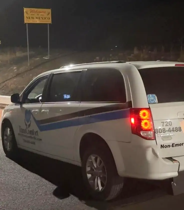 A TransComfort van at the Welcome to New Mexico sign at the state line, photographed at night.