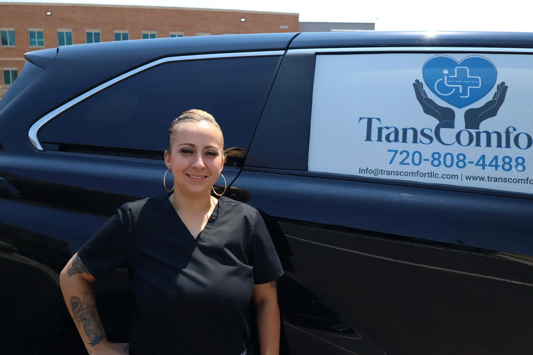 A TransComfort crew member in black scrubs standing beside a van carrying the company logo and phone number.